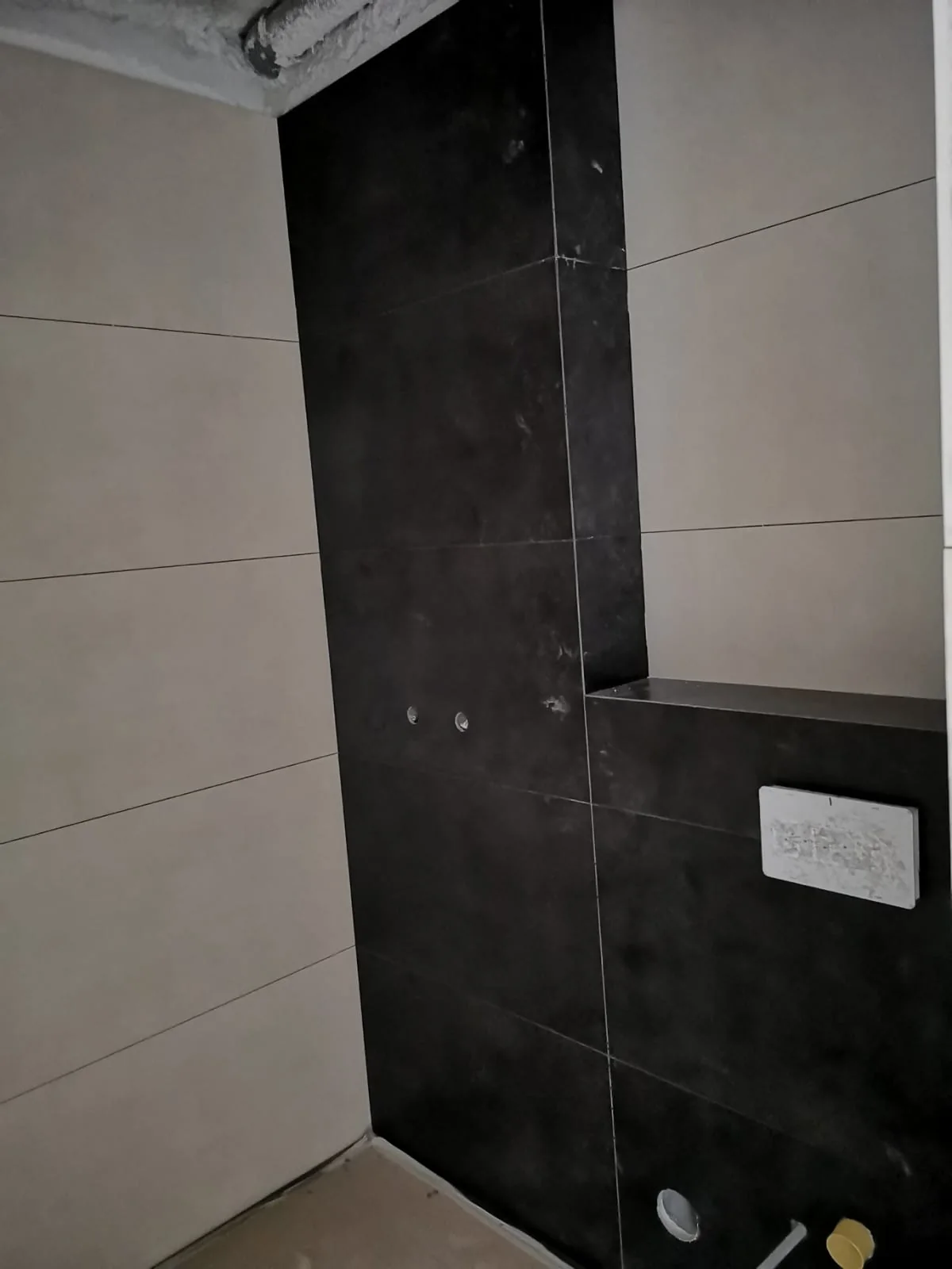 Revestimento de casa de banho em peças claras e escuras, com alinhamento de juntas em execução
