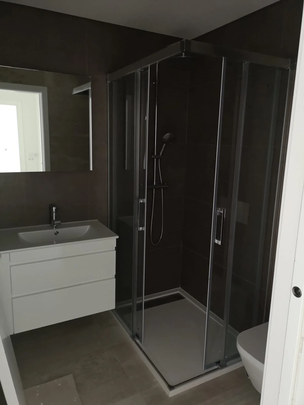 Casa de banho concluída com revestimento escuro na zona de duche e pavimento coordenado
